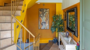 Una escalera con escalones color beige y barandilla amarilla, que lleva a un rellano con una mesa blanca y una puerta verde.
