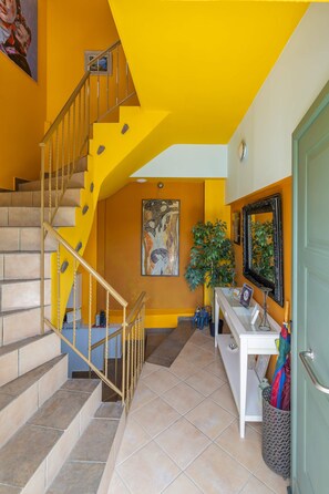 A staircase with beige steps and a yellow handrail, leading to a landing with a white table and a green door. - Phaedra Apartment - Homely Vibes Gem in Kefalonia (Kefalonia)