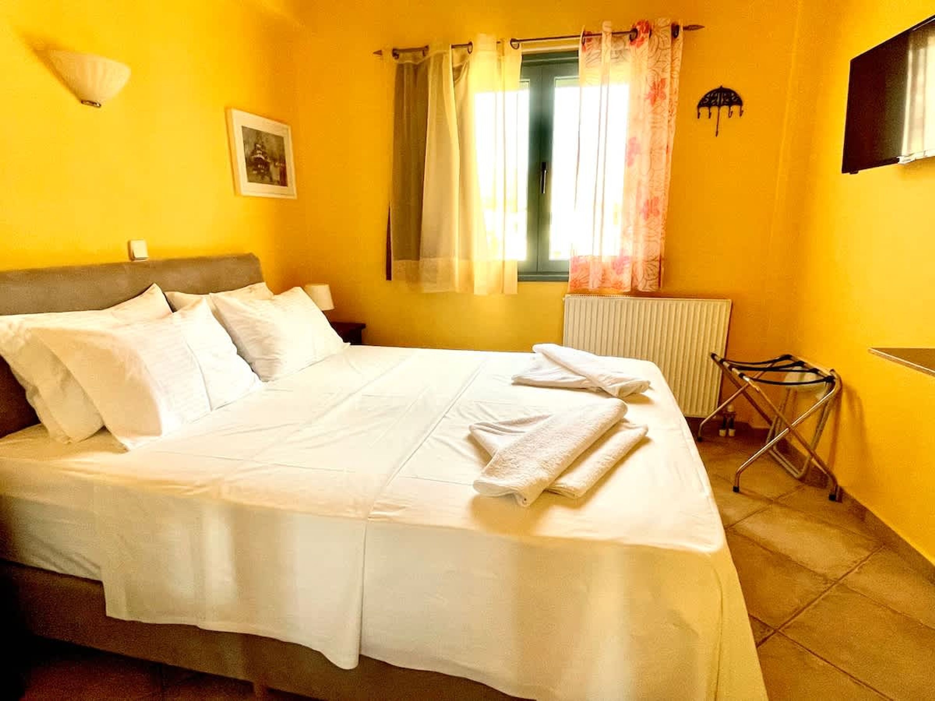 A bed with white linens, a nightstand with a lamp, a radiator, and a window with curtains.