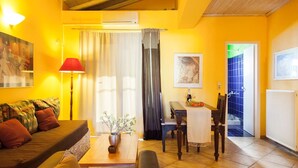 Una sala de estar con un sofá, una mesa con un florero, una lámpara, un comedor con una mesa y sillas, y vistas a una zona azulada con azulejos a través de un umbral.