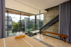 Ein modernes Hotelzimmer mit großem Fenster, einer hölzernen Bank und Blick auf die Stadtlandschaft.