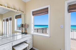 Ein Badezimmer mit einem großen Spiegel, einem Schminktisch mit Schubladen, einem Fenster mit Meerblick und einer Tür, die auf einen Balkon führt.