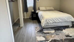 Un dormitorio con una cama, una ventana con cortinas, una mesita de noche y una alfombra.