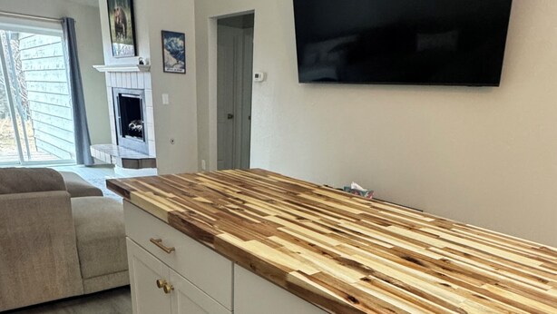 Una cocina con encimera de madera, armarios blancos y un televisor de pantalla plana montado en la pared.