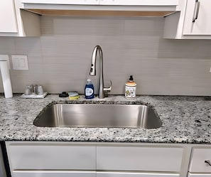 Eine Küche mit einer Edelstahl-Spüle, einem Wasserhahn, einer Seifenspender und einer Flasche Geschirrspülmittel.