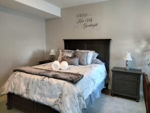 Ein Schlafzimmer mit Bett, Kissen, Nachttisch und einer Wandtafel.