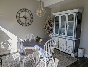 Un coin repas avec une table ronde, des chaises blanches, une horloge décorative, un luminaire suspendu et un meuble avec des portes en verre.