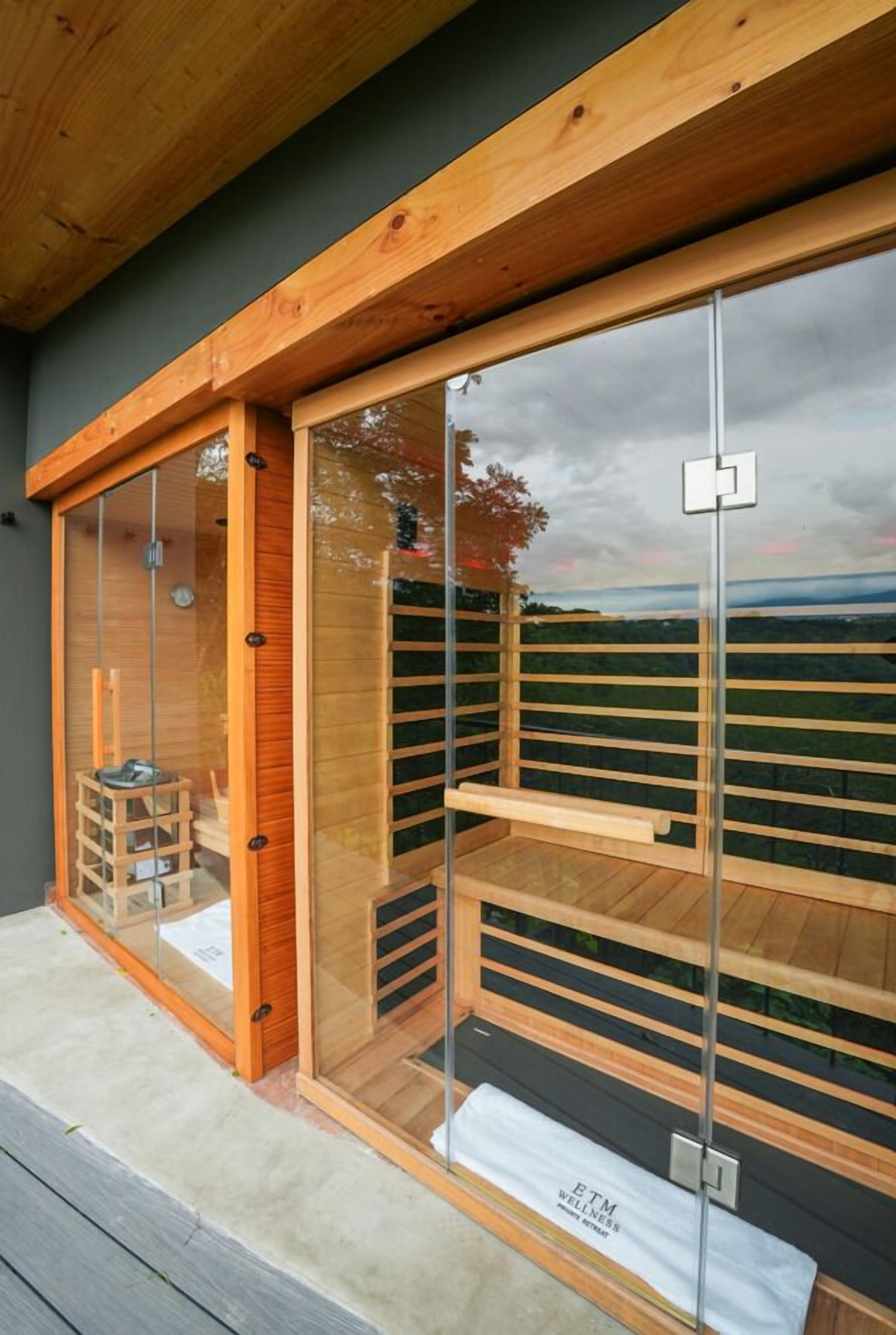 A modern wooden structure with glass walls, a bench, and a view of a landscape.