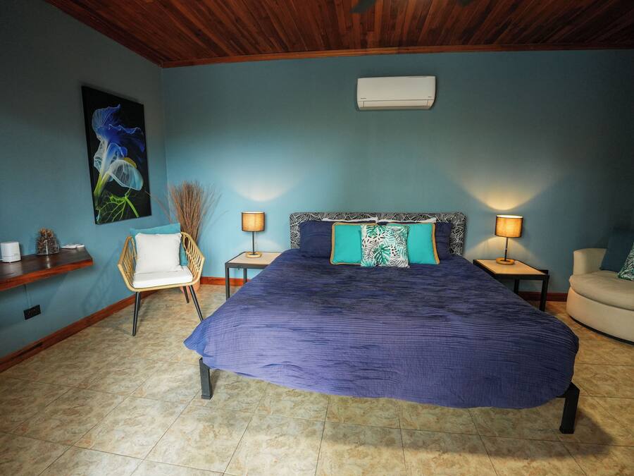 Un dormitorio con una cama grande, dos mesitas de noche, una silla y un aire acondicionado de pared.