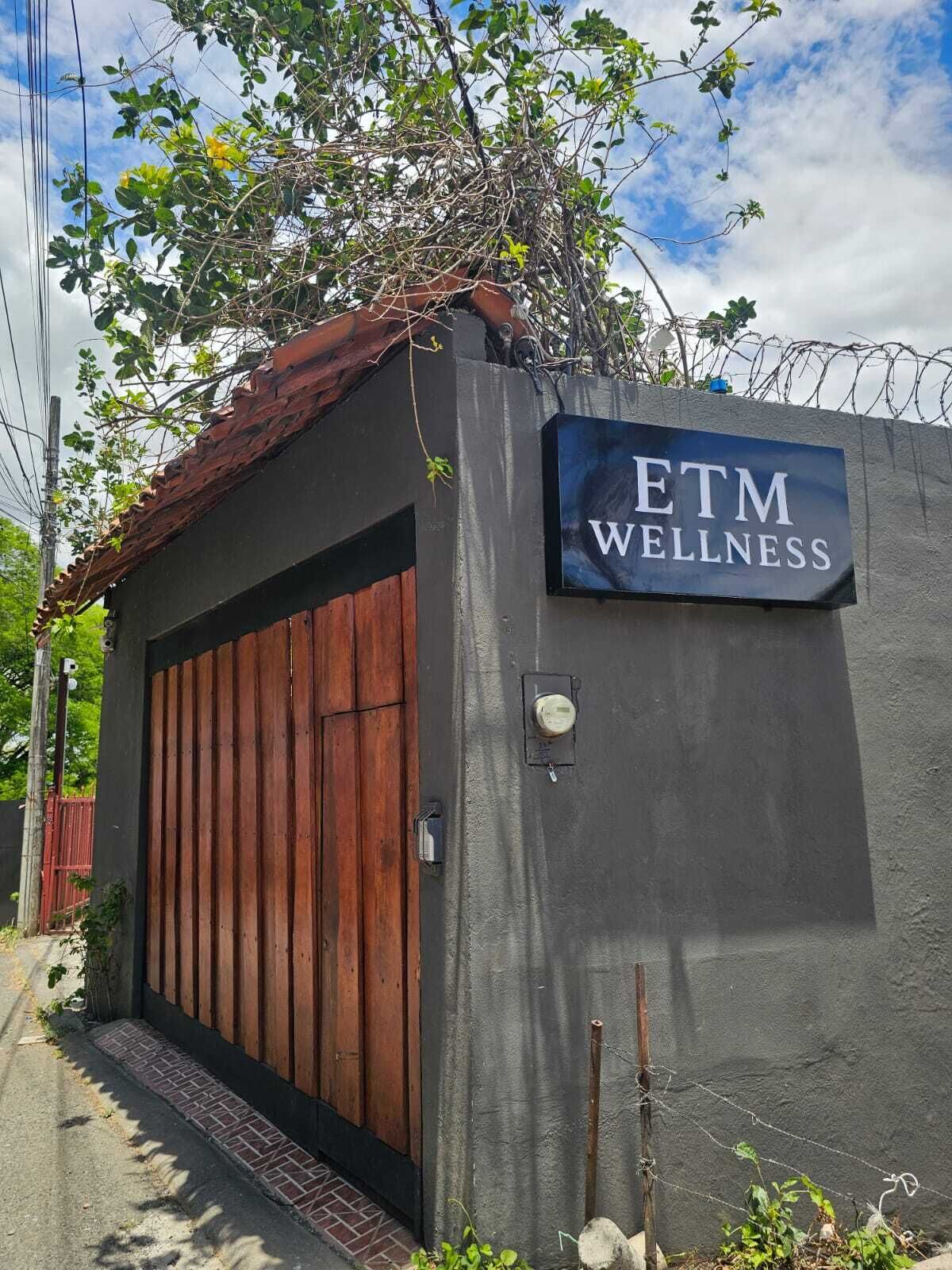 Un centre de bien-être fermé par un portail, avec une enseigne indiquant « ETM WELLNESS » sur un mur gris.