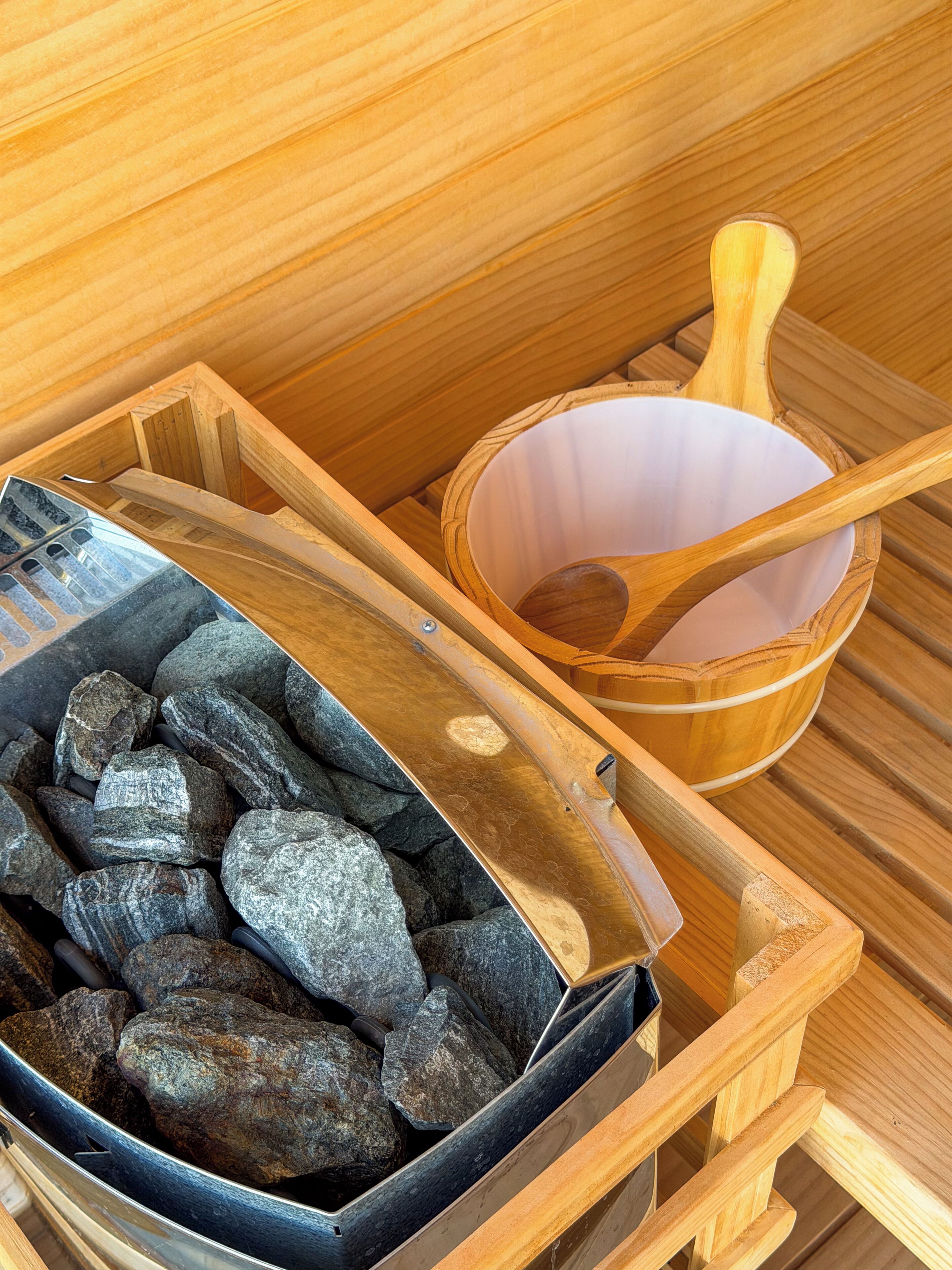 A sauna with wooden benches, a wooden bowl, and a container of rocks.