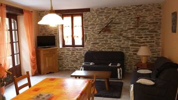 A living room with a stone wall, a sofa, a dining table, and a television.