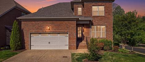 A two-story brick house with a garage, a small porch, and a well-maintained lawn.
