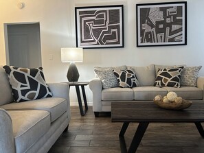Una sala de estar con un sofá, dos almohadones estampados, una mesita de noche con lámpara y una mesa de centro con esferas decorativas.