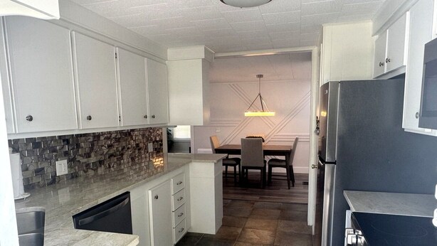 A modern kitchen with white cabinets, a tiled backsplash, a built-in dishwasher, and a stainless steel refrigerator. - Spacious Furnished Retreat- Perfect for Extended Stays (Venice)