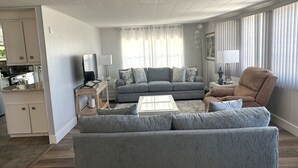 A living room with a grey sofa, a brown armchair, a coffee table, and a TV on a stand. - Spacious Furnished Retreat- Perfect for Extended Stays (Venice)