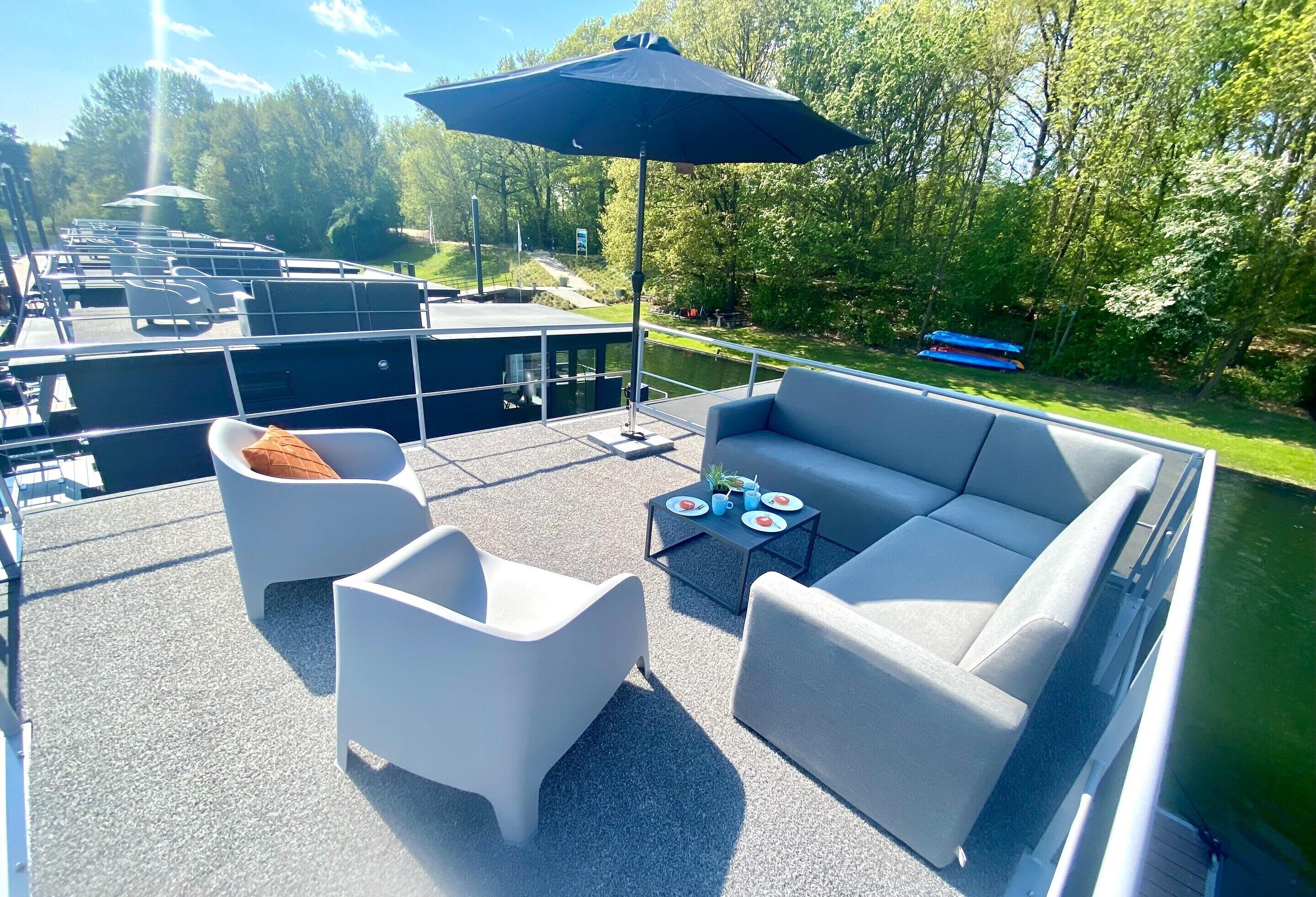 Een terras met buitenmeubilair, een tafel met een drankje en uitzicht op een rivier.