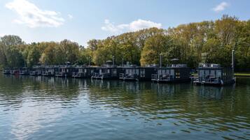 A row of floating structures with outdoor seating areas, connected by walkways, set against a backdrop of trees and a clear sky.