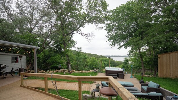 Une terrasse en bois avec coin salon extérieur, un jacuzzi et une vue sur un lac.