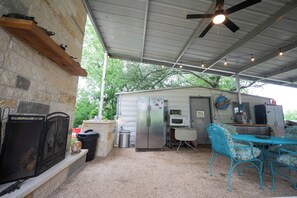 A covered outdoor area with a stone wall, a metal ceiling fan, string lights, a refrigerator, a microwave, a table with chairs, and a small shed. - Lake Belton Boho Escape - ADA Ramps + RV Parking (Temple)