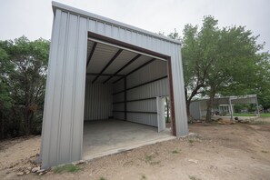 A metal building with an open door, surrounded by trees and a dirt ground. - Lake Belton Boho Escape - ADA Ramps + RV Parking (Temple)