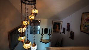 Une pièce avec un luminaire décoratif suspendu, un tableau encadré au mur et une petite étagère sur laquelle sont posés divers objets.