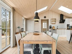 Una cocina amplia con una mesa de madera, armarios blancos y una lámpara colgante negra.