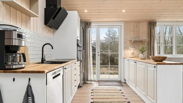 A modern kitchen with white cabinetry, a coffee maker, and a view through a glass door. - "Martta" - 250m from the sea by Interhome (Knebel)