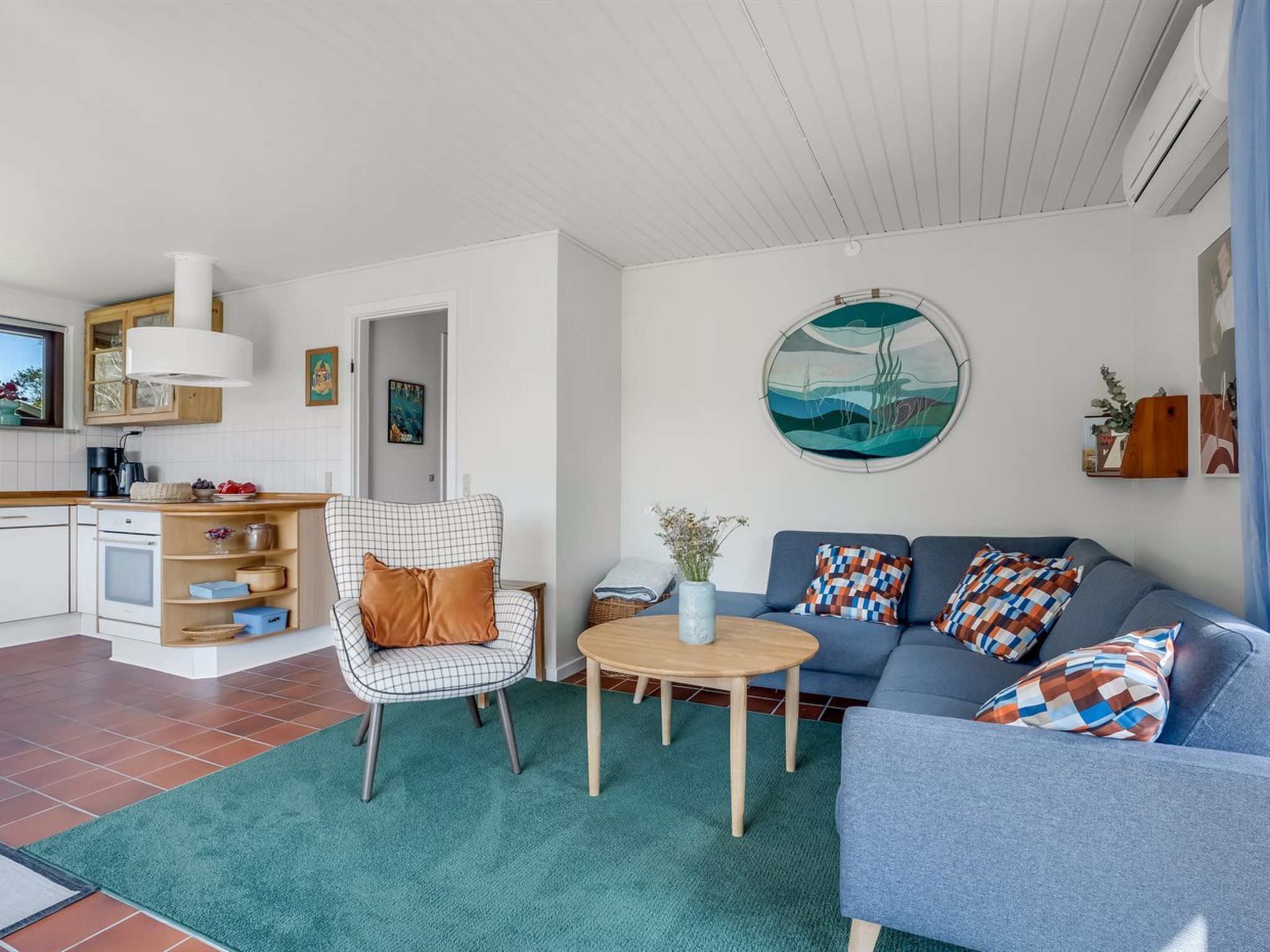 A modern living room with a sofa, armchair, and coffee table. There is a kitchen area with cabinets and a stove.