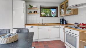 Eine kompakte Küche mit weißen Schränken, einer Holzarbeitsplatte, einem Fenster mit Blick und einem Essbereich mit Tisch und Stühlen.