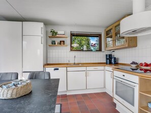 Ett kompakt kök med vita skåp, en bänkskiva i trä, ett fönster med utsikt och en matplats med ett bord och stolar.