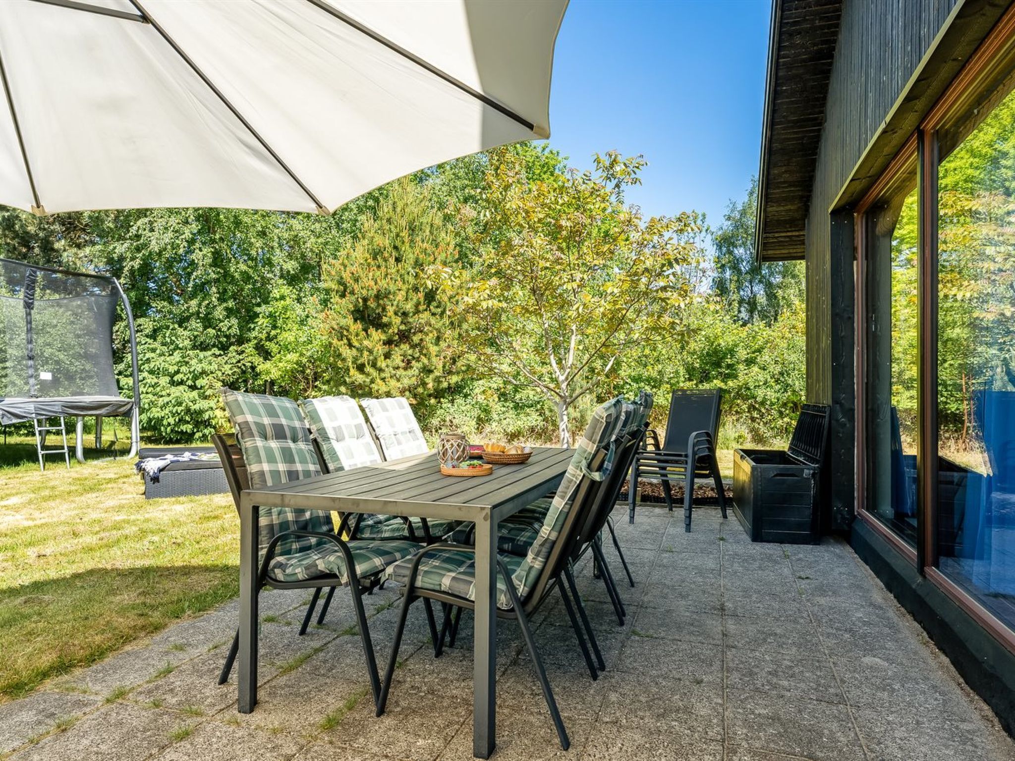 Une terrasse extérieure avec une table et des chaises, un trampoline et un grand parasol.