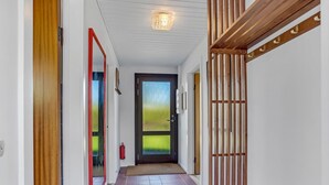 Ein Flur mit einer hölzernen Sitzbank, einer Tür mit satinierten Glasscheiben und einem Feuerlöscher an der Wand.