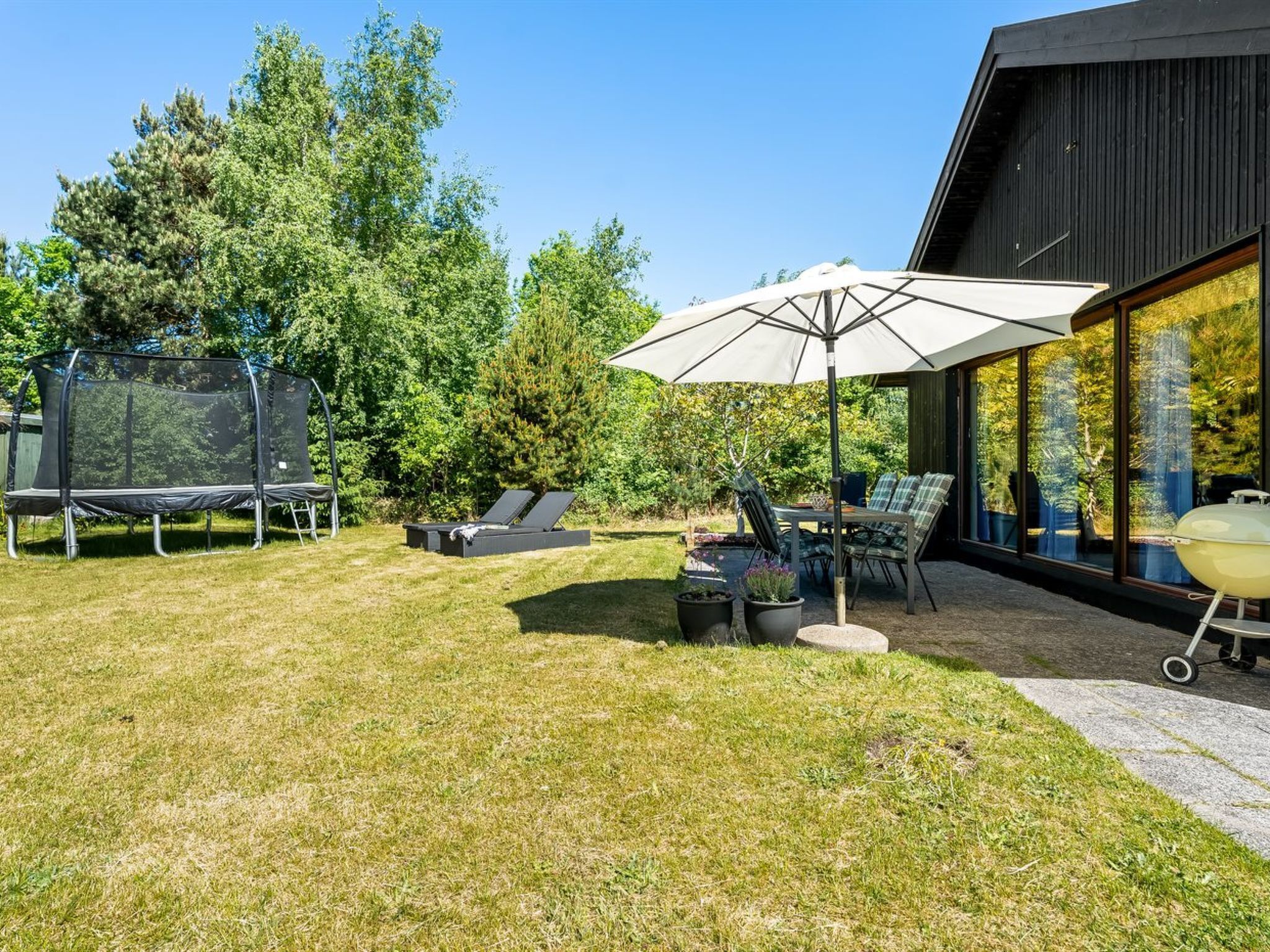 A backyard with a trampoline, outdoor seating, and a large umbrella.
