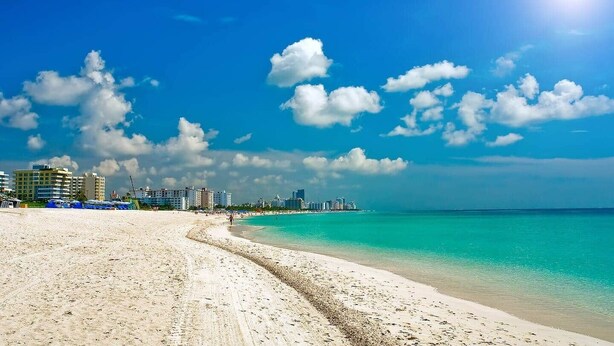 A beach with a clear sky, a sandy shore, and buildings in the background. - 1128 - Ocean View with Balcony (Miami Beach)