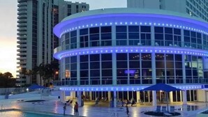 A modern building with a curved facade, large windows, and a pool area with umbrellas. - 1128 - Ocean View with Balcony (Miami Beach)