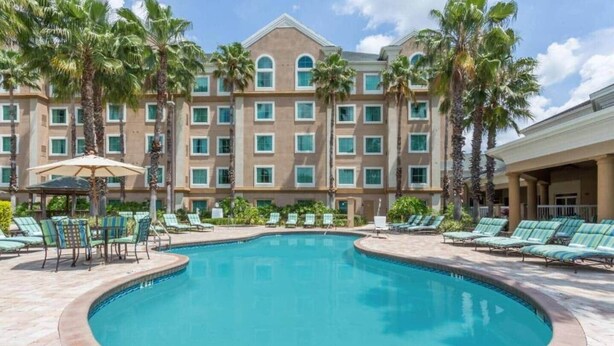 A hotel with a swimming pool, palm trees, and lounge chairs. - 110 - Next to Disney - Pool (Orange County)