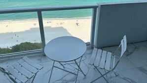 Ein Balkon mit Blick auf den Strand, einem runden Tisch und zwei weißen Liegestühlen.