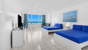 A hotel room with a bed, a desk, a chair, a table, and a view of the sea. - 530 - Large Studio Ocean View (Miami Beach)