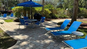 A patio area with blue lounge chairs, a round table, and a blue umbrella. - 510 - Oasis in Disney world (Orange County)