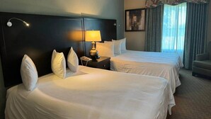 A hotel room with two beds, a nightstand with a lamp, a chair, and a window with curtains. - 510 - Oasis in Disney world (Orange County)