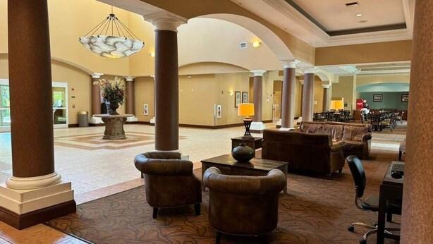 A spacious lobby with a high ceiling, large columns, and a central chandelier. There are leather sofas and a wooden coffee table. - 510 - Oasis in Disney world (Orange County)