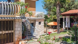 A two-story house with a stone facade, a balcony with a railing, and a garden with various plants and flowers. - Cozy Holiday Studio in Umag (Umag)