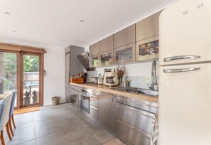 Eine moderne Küche mit Edelstahlgeräten, einem Holzessttisch und einer Schiebeglasdoor zum Außenbereich.