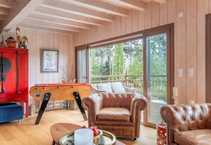 Ein gemütliches Zimmer mit Poolbillard, Ledersofas und einem großen Fenster mit Blick auf Bäume.