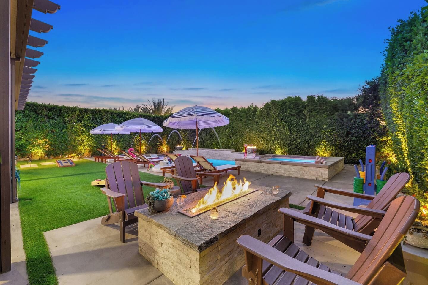 An outdoor patio with a fire pit, lounge chairs, and umbrellas.