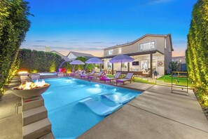 Une piscine entourée d’une maison et de verdure, avec des chaises longues et des parasols.