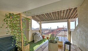 Eine Dachterrasse mit einer Holzpergola, Kübelpflanzen, einer kleinen Sitzecke und Blick auf die Stadtlandschaft.