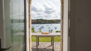 A view through an arched doorway to a patio with a table and chairs, overlooking a body of water with boats. - Beautiful Panoramic View of the sea - Portsall (Ploudalmezeau)