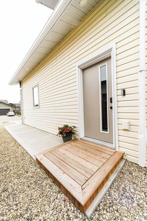A house with a front porch, a door, and a small garden area with a planter. - Modern Comfort in Westgate (Grande Prairie)